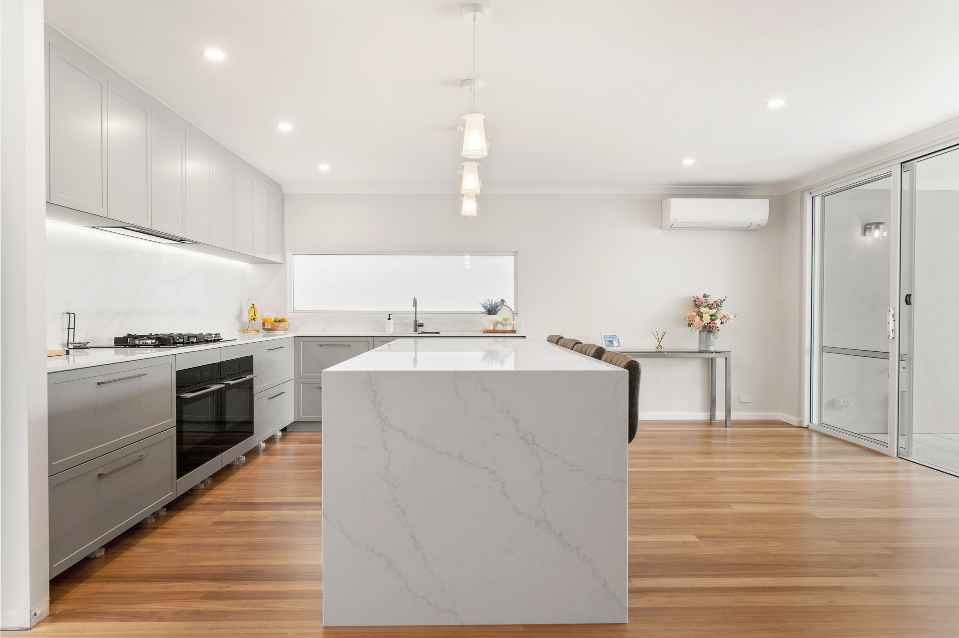 a newly renovated kitchen showing the kitchen counter, cupboards and oven along the left side, and polished wood floors.